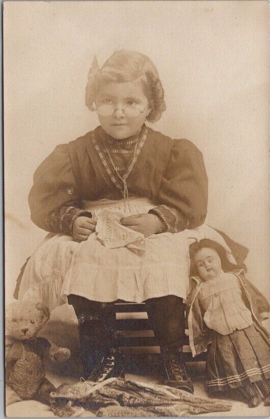 c1910s Studio Photo RPPC Postcard Little Girl with Glasses, Teddy Bear & Doll