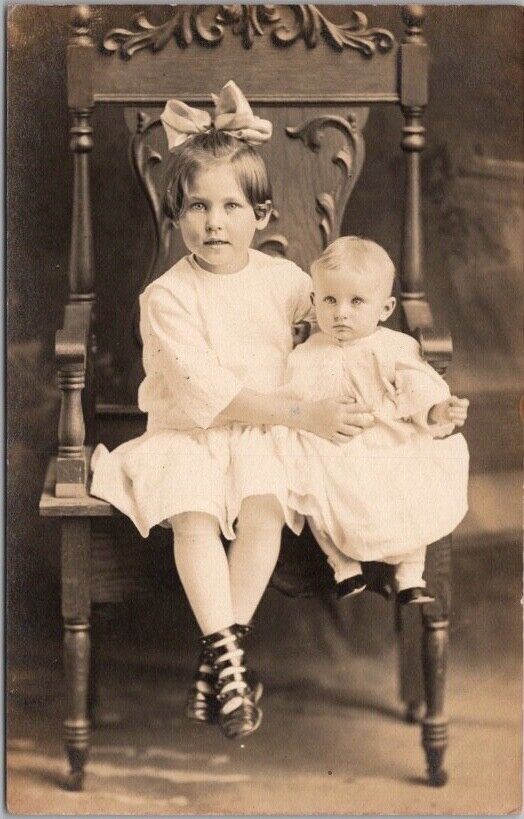 c1910s STUDIO Photo RPPC Postcard Cute Little Girl Holding up Baby on Big Chair
