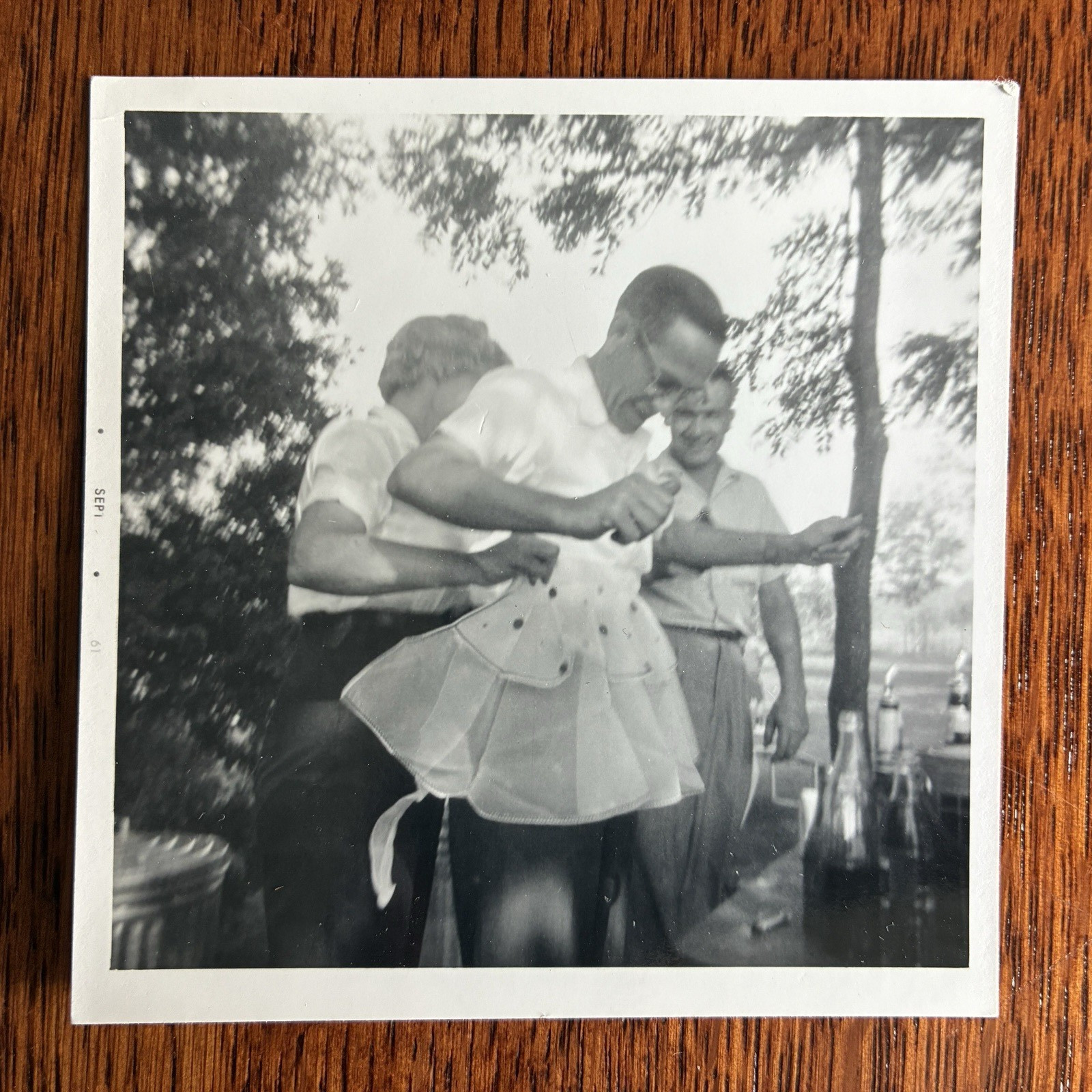 Comical lady tries apron cross dress on smiling man liquor bottle drunken picnic