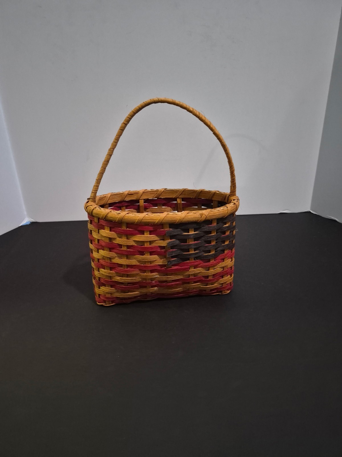 Handmade woven reed basket featuring a tan, red, Blue with single arched handle Handmade woven reed basket featuring a tan, red, Blue with single arched handle