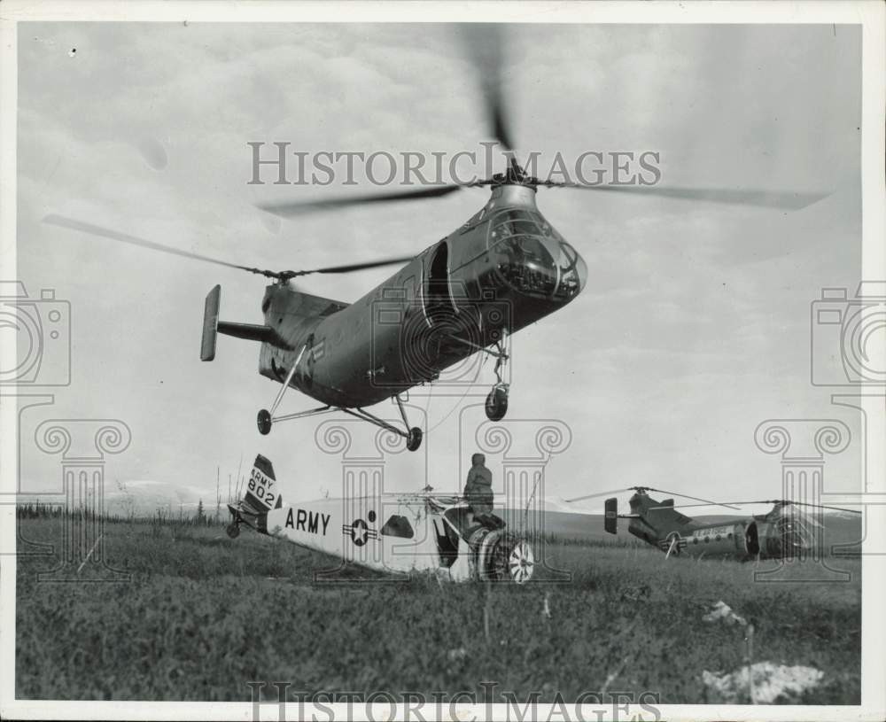 1957 Press Photo A H-21B helicopter lifted a small Army plane in the field 1957 Press Photo A H-21B helicopter lifted a small Army plane in the field