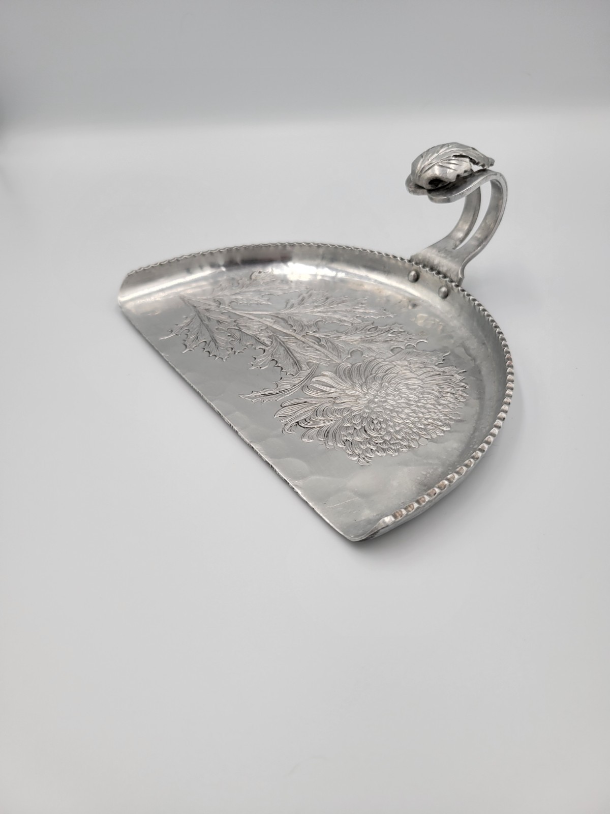 Hand-wrought aluminum crumb catcher with decorative chrysanthemum relief pattern