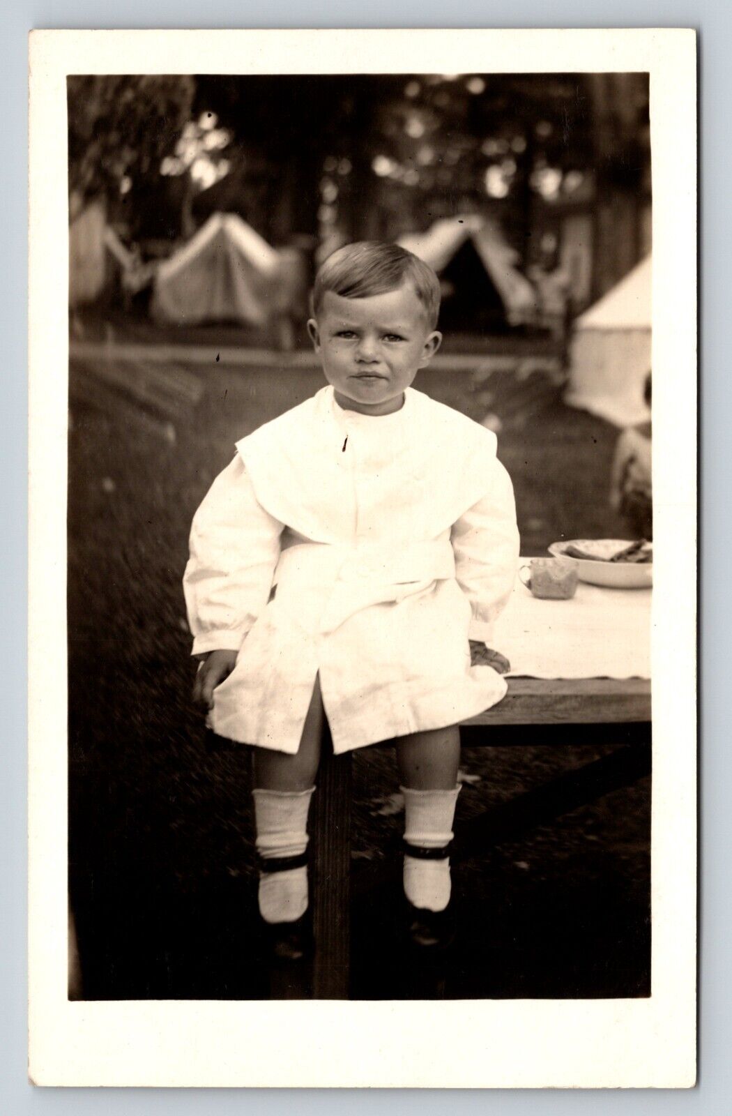 c1915 RPPC Postcard: Kid Sits On A Table, Tents In The Background - Summertime