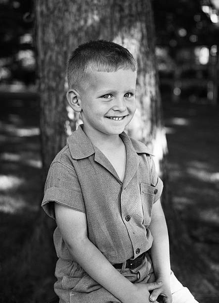 Smiling portrait of a smiling boy seated before a tree trunk 1930 Old Photo
