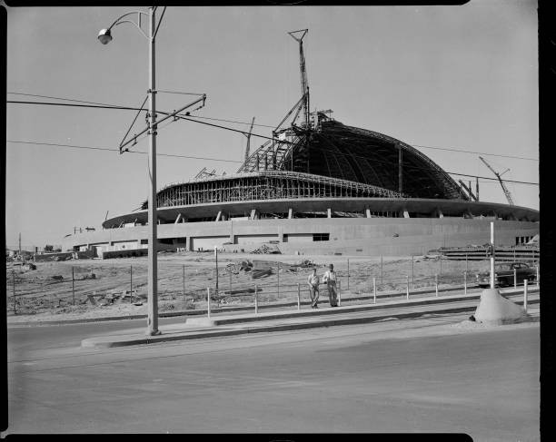 Two men leaning fence front of Civic Arena construction partially - Old Photo