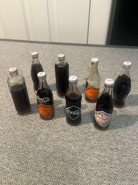 8 Miniature Coca Cola Bottles Depicting Different Eras of Coke Bottles