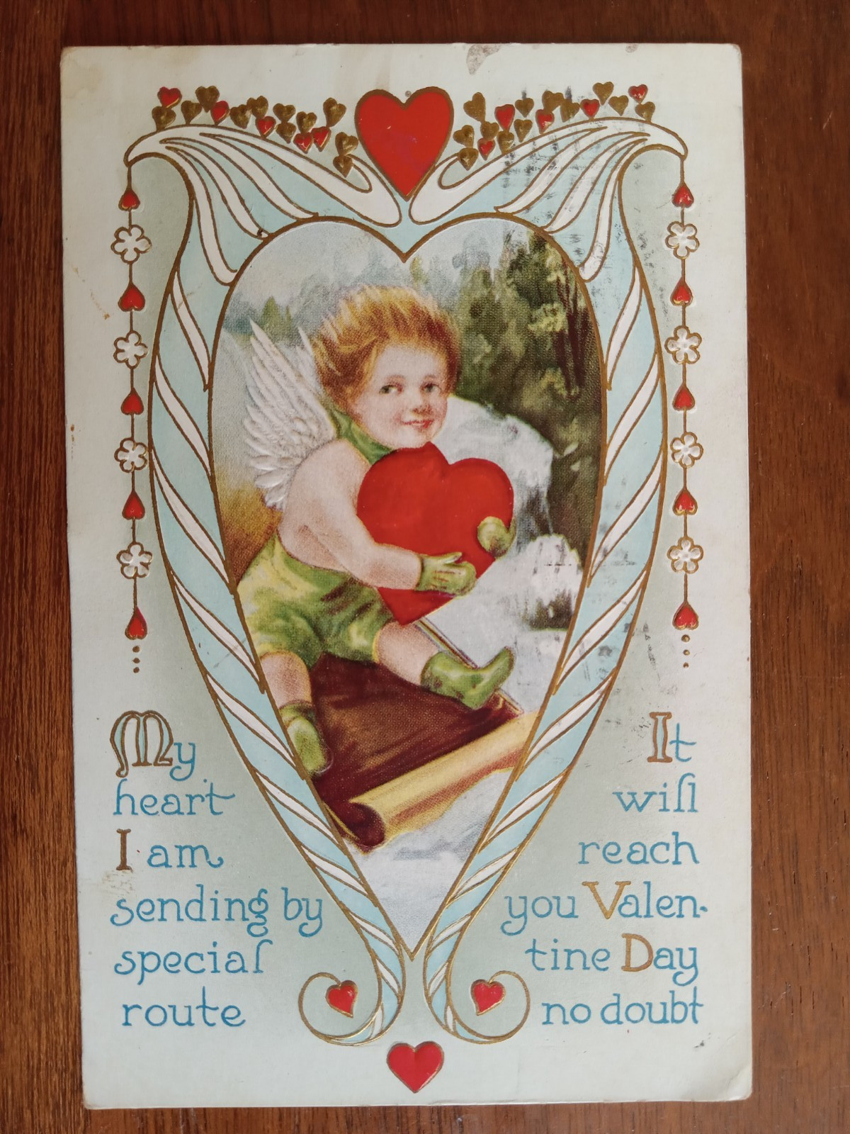 c1913 Embossed Valentine, Cupid on toboggan, hearts, gilt, verse