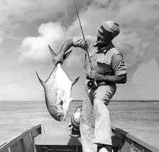Joe Brooks stands a small wooden boat holding a permit caught fly - Old Photo picture