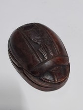 A collectible scarab made of carved dark brown stone featuring an Egyptian style picture